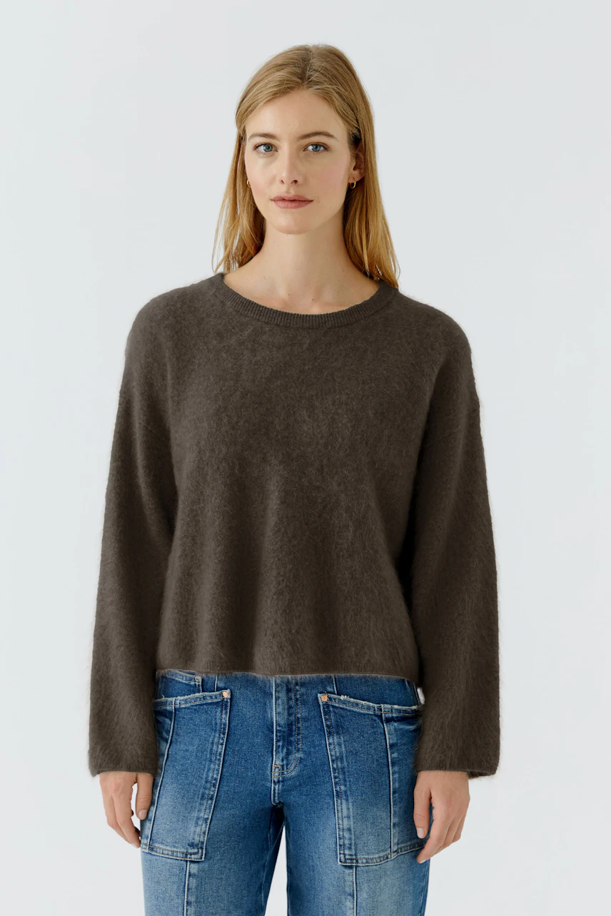 Casual pullover: Woman in a cozy brown pullover and blue jeans, standing confidently.
