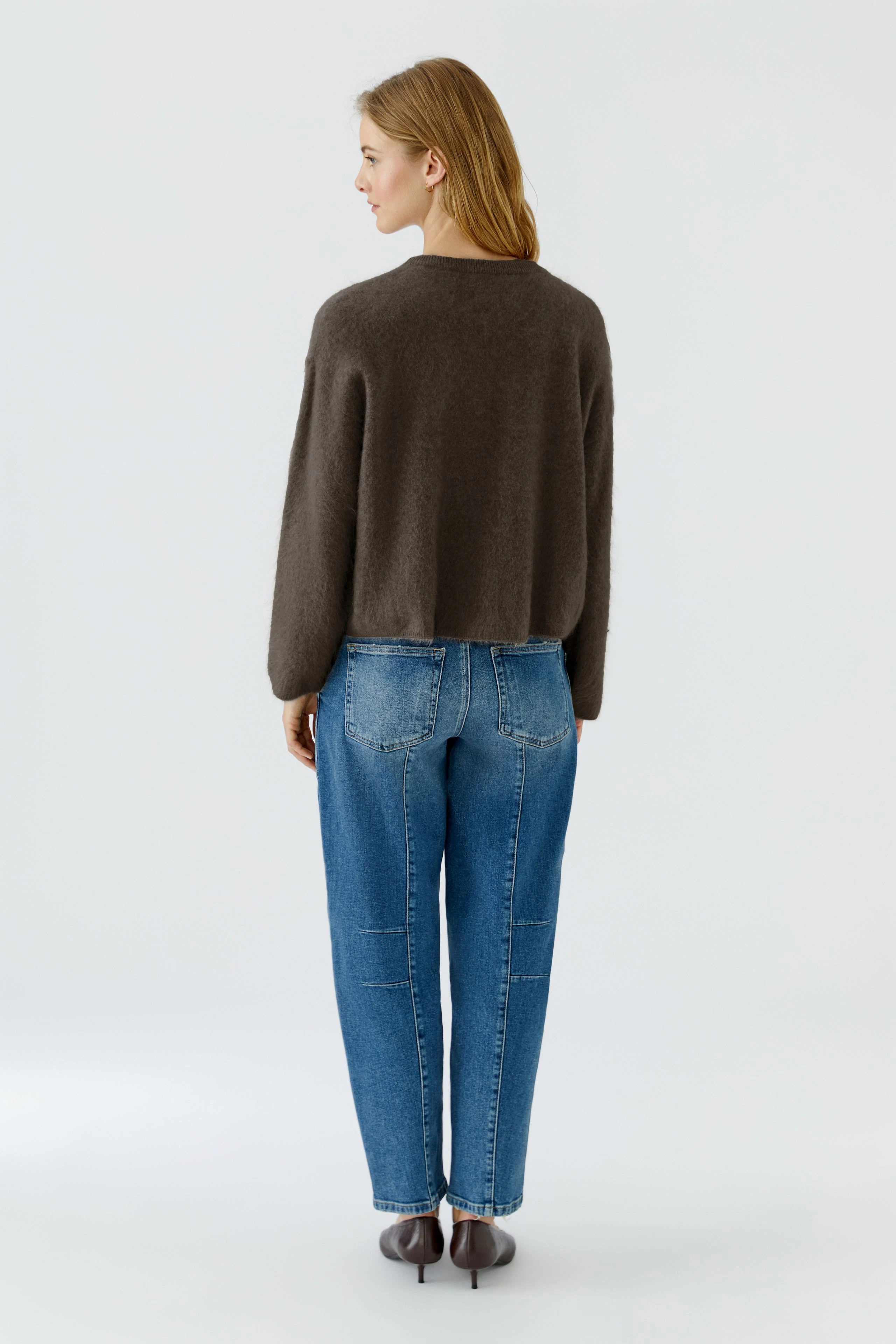 Lässiger Damen-Pullover: Frau im braunen Pullover und blauer Jeans von hinten, entspannt und modern.