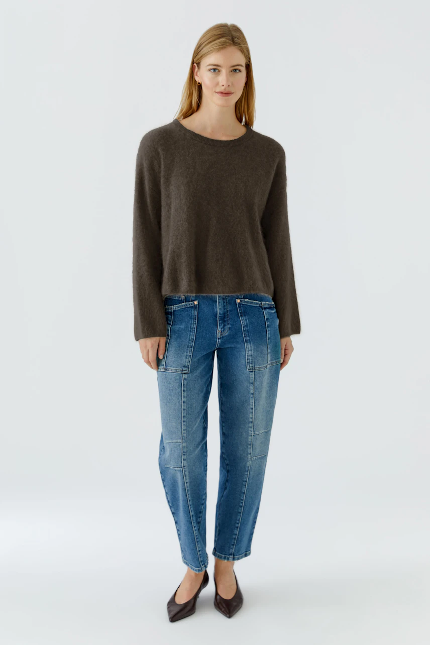 Casual women's pullover: Woman in a brown pullover and blue jeans stands confidently.