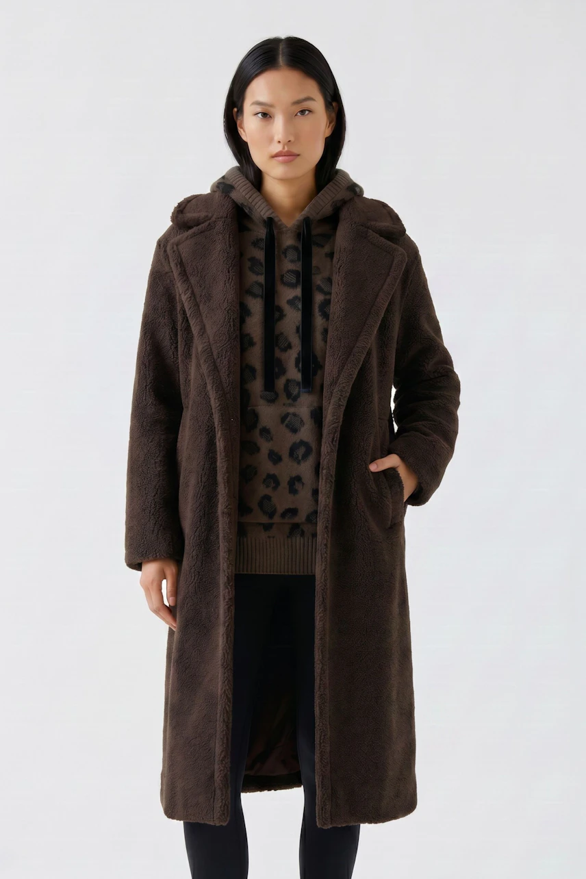 Woman in a cozy winter coat over a leopard print hoodie, hands in pockets, standing confidently.