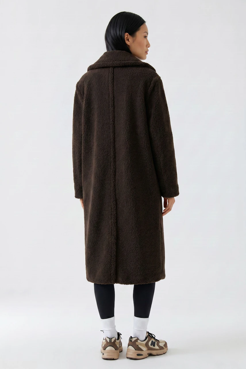 Cozy winter coat: Woman in a long, brown coat with a relaxed fit, paired with leggings and sneakers.