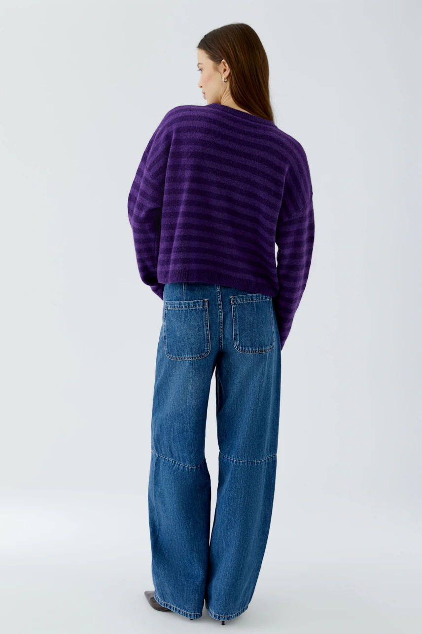 Lässiger Damen-Pullover: Frau im lila Pullover und blauer Jeans von hinten, entspanntes Outfit.