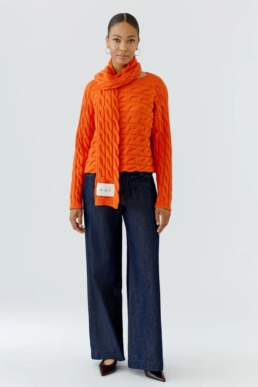 Frau mit orangefarbenem Schal und passendem Pullover, kombiniert mit dunkelblauer Hose.