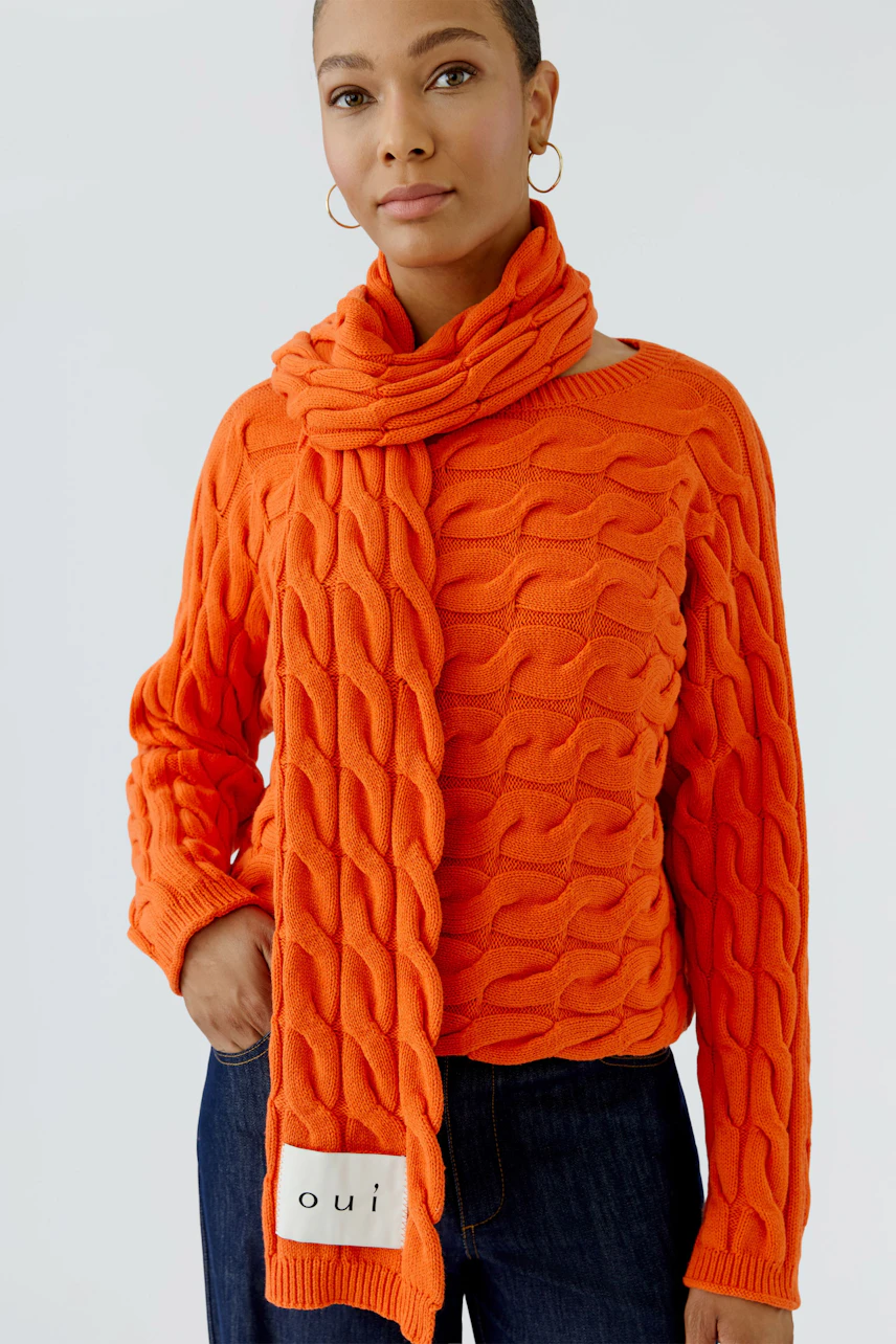 Frau mit orangefarbenem Schal und passendem Pullover, lässig kombiniert mit Jeans.