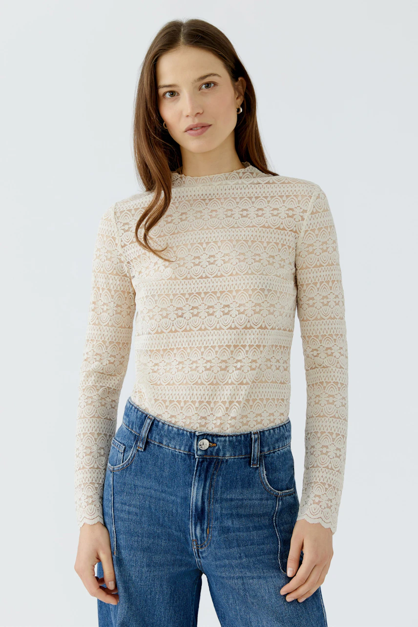 Casual long-sleeve shirt: Woman in a lace-patterned shirt and jeans, standing confidently.