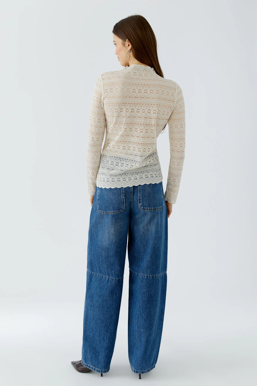 Casual long-sleeve shirt: Woman in a patterned beige shirt and wide blue jeans, viewed from the back.