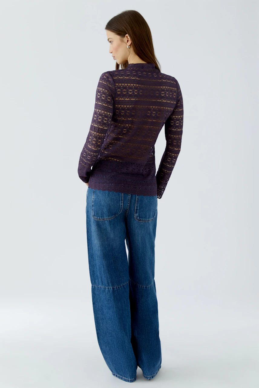 Woman in a patterned long-sleeve shirt and wide-leg jeans, viewed from the back.