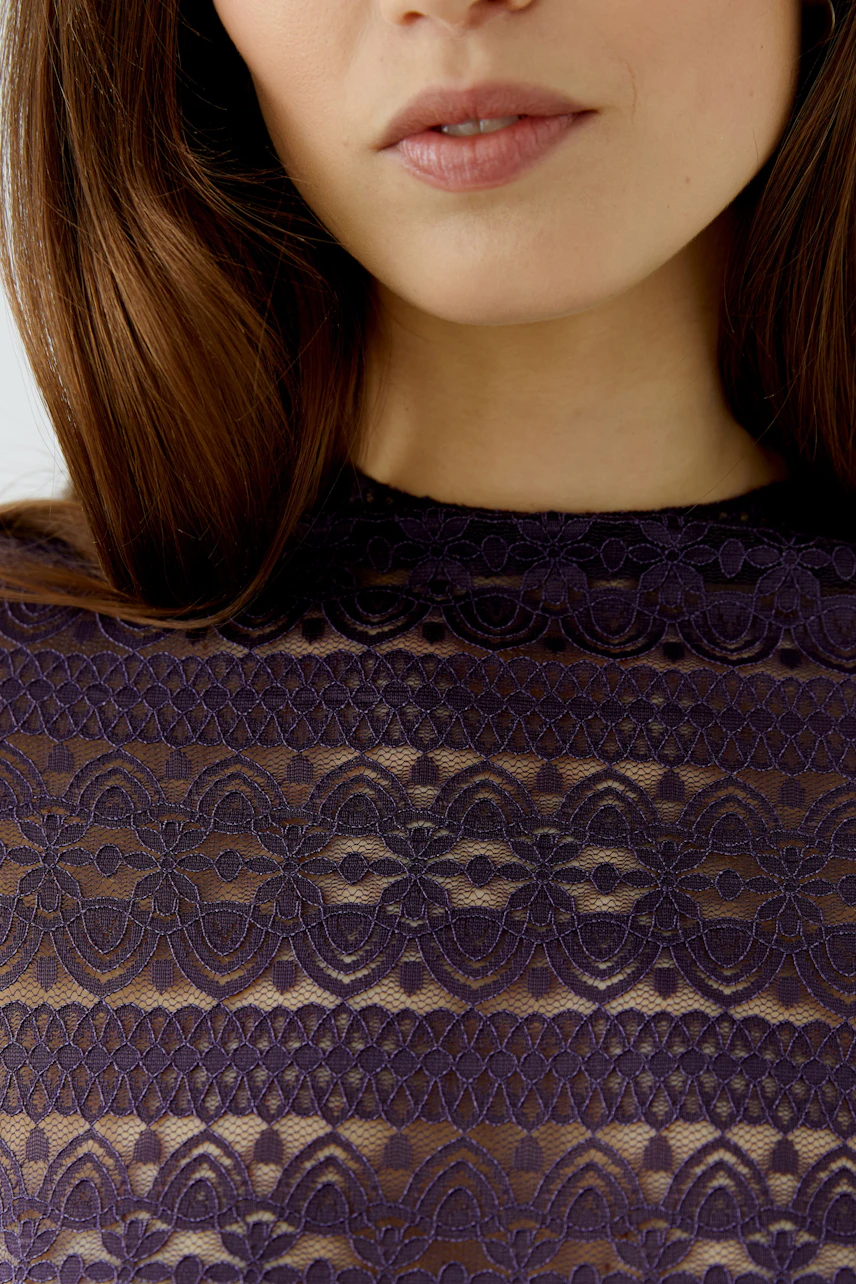 Woman in a lace long-sleeve shirt, close-up of intricate purple pattern, showcasing delicate design.