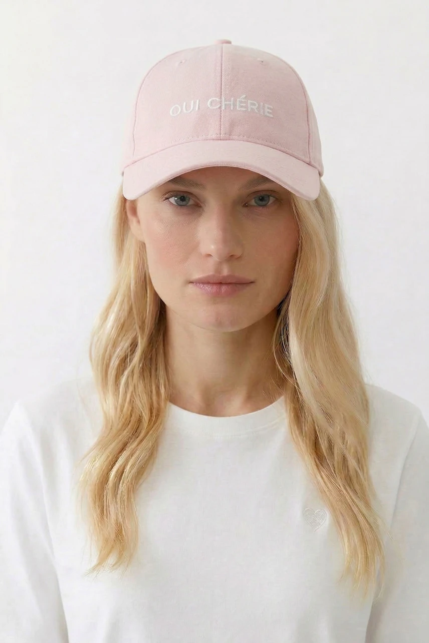 Lässiger Damen-Hut: Frau mit rosa Cap und "Oui Chérie" Schriftzug, trägt weißes Shirt.