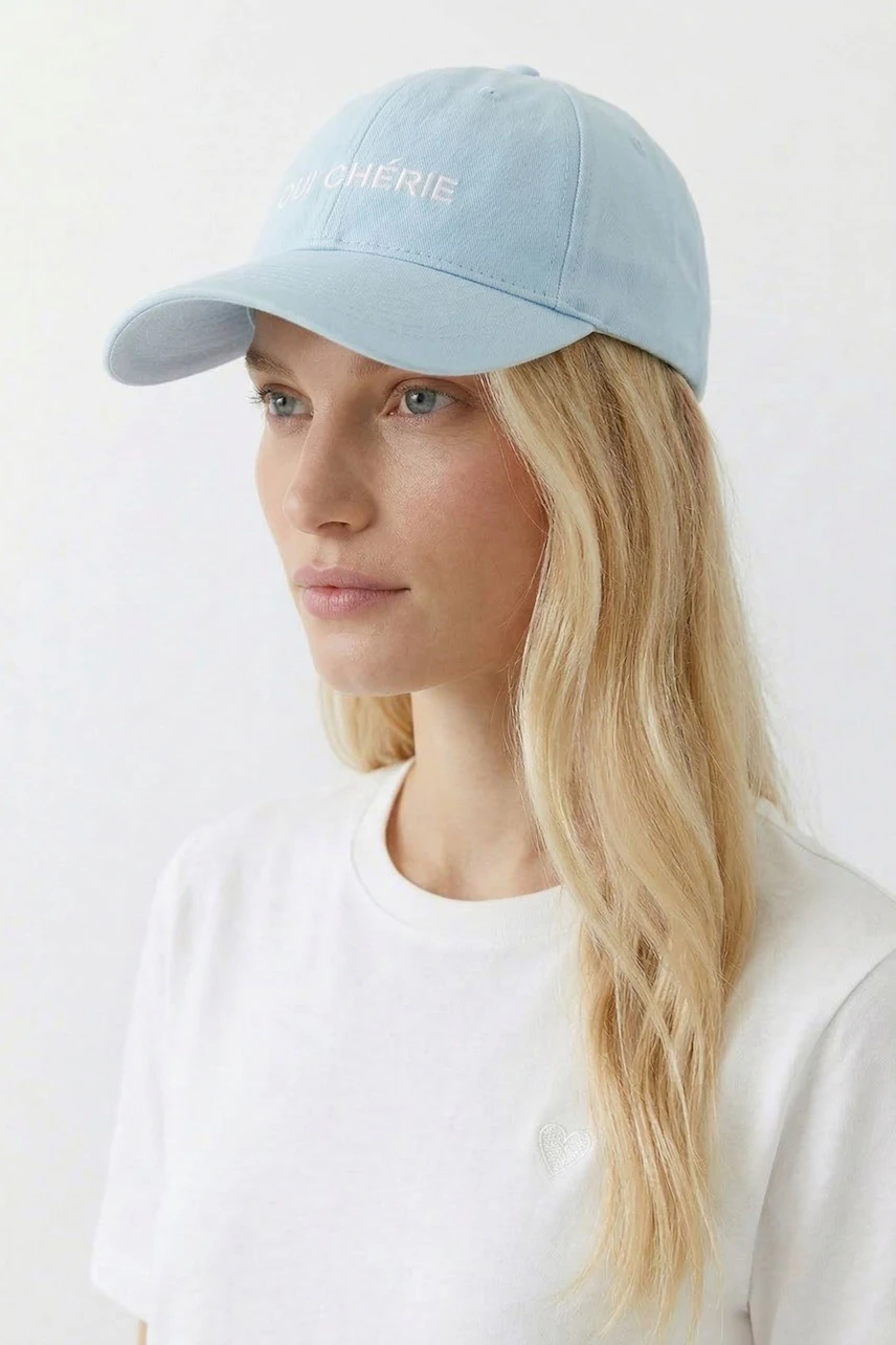 Lässiger Damen-Hut: Frau mit hellblauer Kappe und weißem T-Shirt blickt zur Seite.