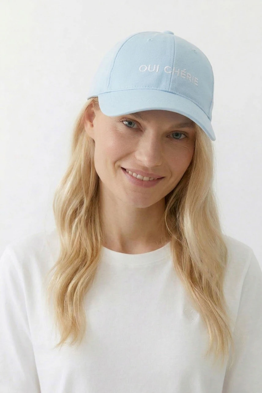 Lässiger Damen-Hut: Frau mit hellblauer Kappe und weißem Shirt lächelt freundlich.