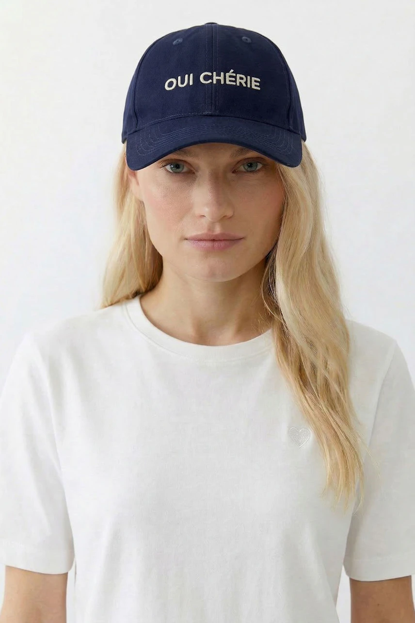 Damen-Hut: Frau mit blauem Hut "Oui Chérie" und weißem T-Shirt blickt direkt in die Kamera.
