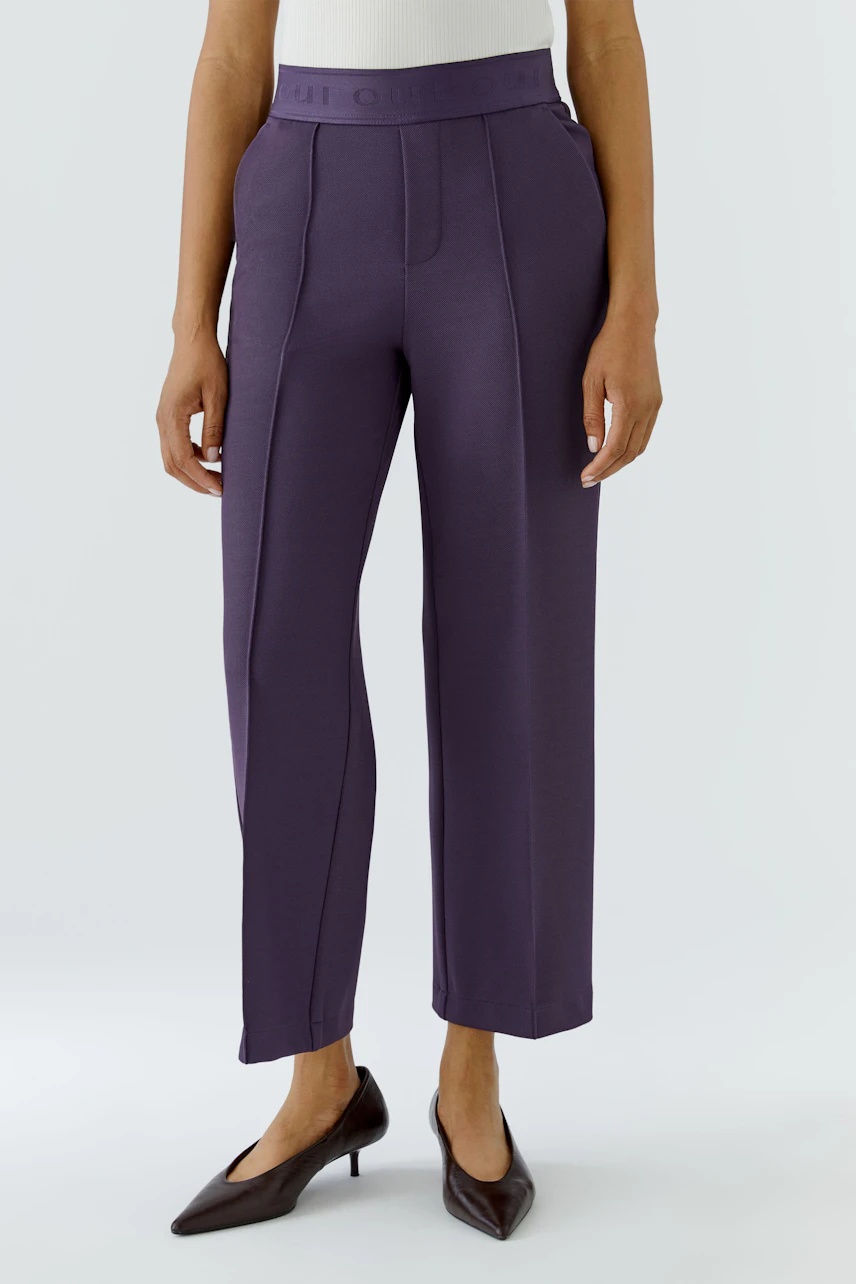 Frau in lila Culotte: Bequeme, weite Hose mit hohem Bund, kombiniert mit schlichten Pumps.