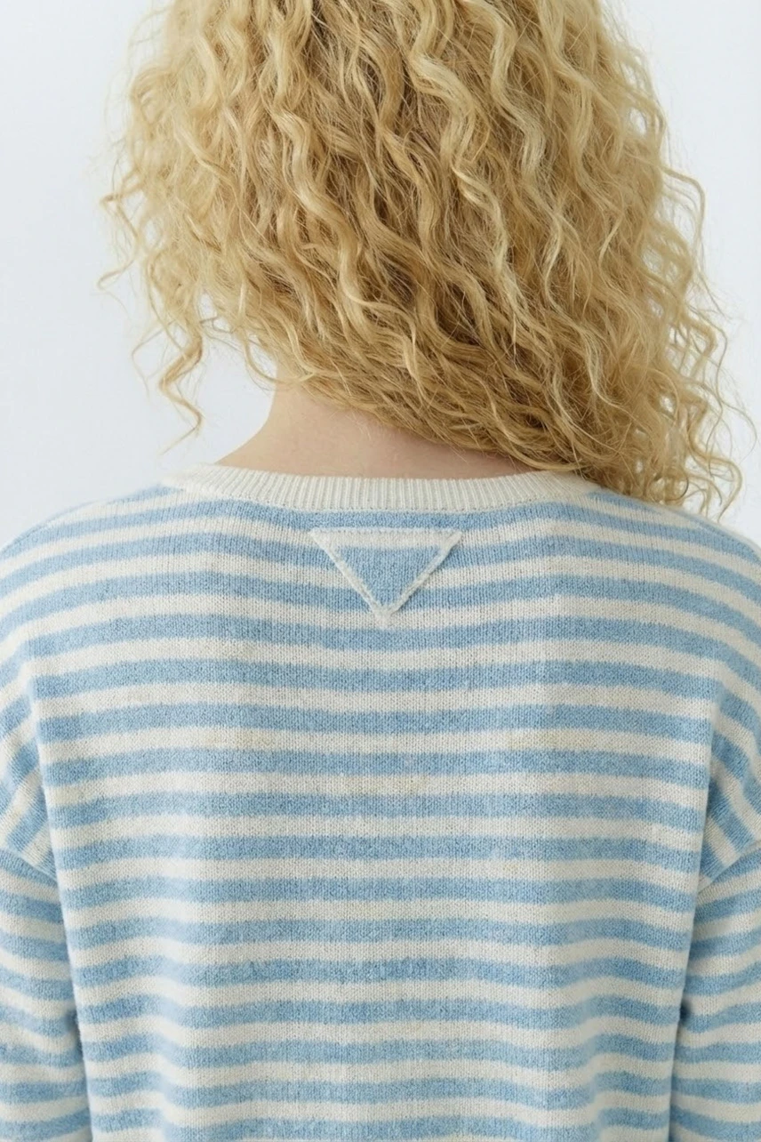 Damen-Pullover: Frau mit lockigen Haaren trägt einen gestreiften Pullover in Blau und Beige.