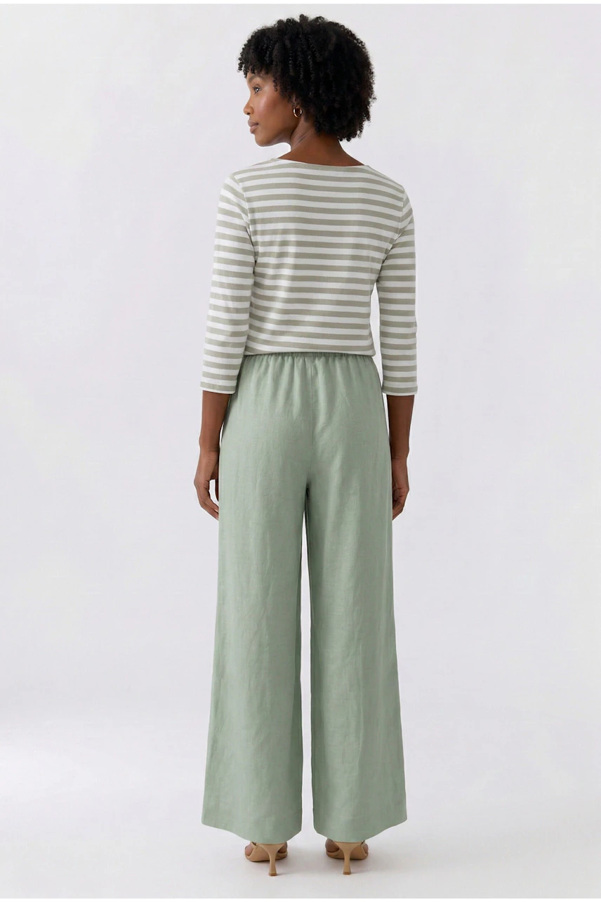 Frau in grüner Marlenehose und passendem Oberteil, Rückansicht. Lässiger Look mit weitem Schnitt.