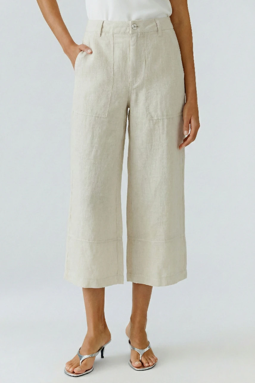 Casual women's pants: Woman in beige wide-leg pants with a white top and silver sandals, standing confidently.