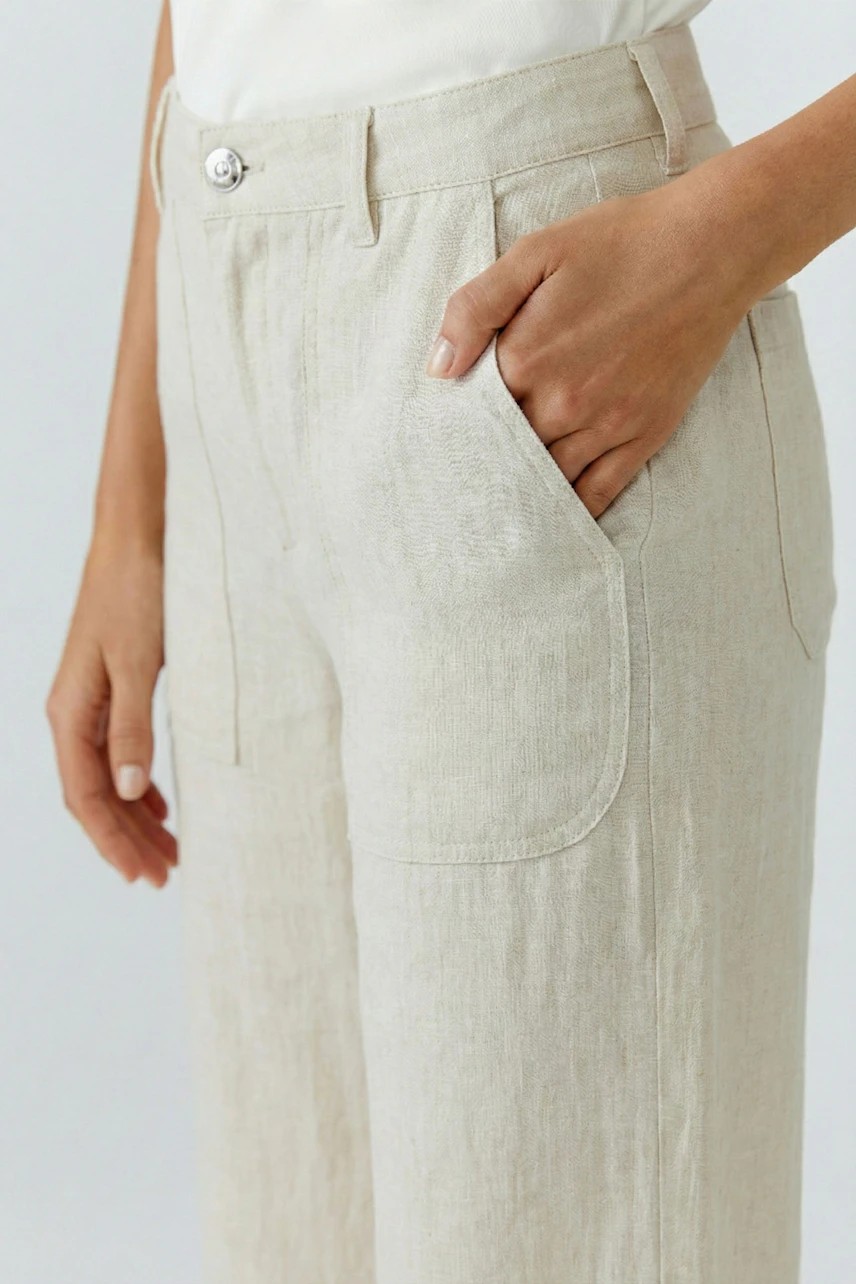 Casual women's pants: Woman in beige linen pants with a relaxed fit, hand in pocket, wearing a white top.