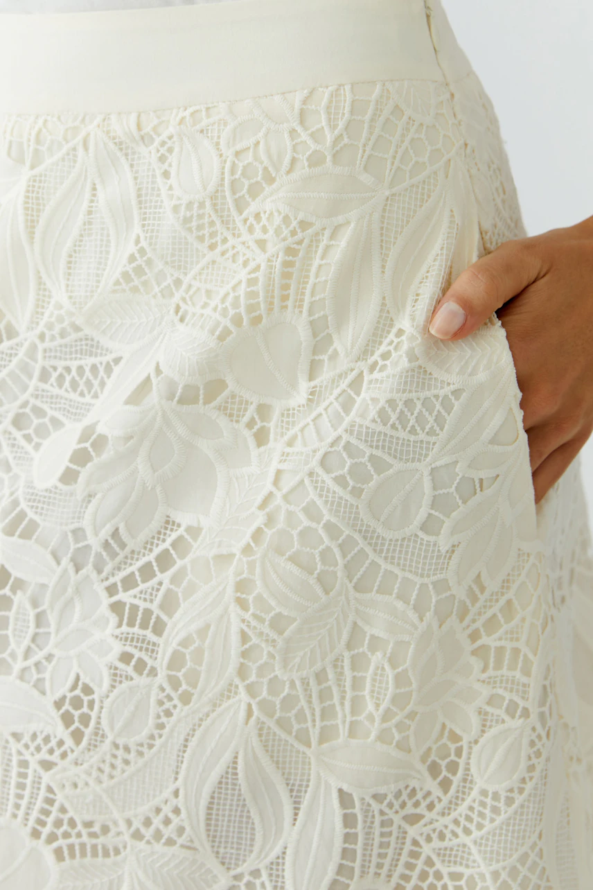 A-line skirt: Close-up of a woman’s hand on a white lace skirt with floral patterns.