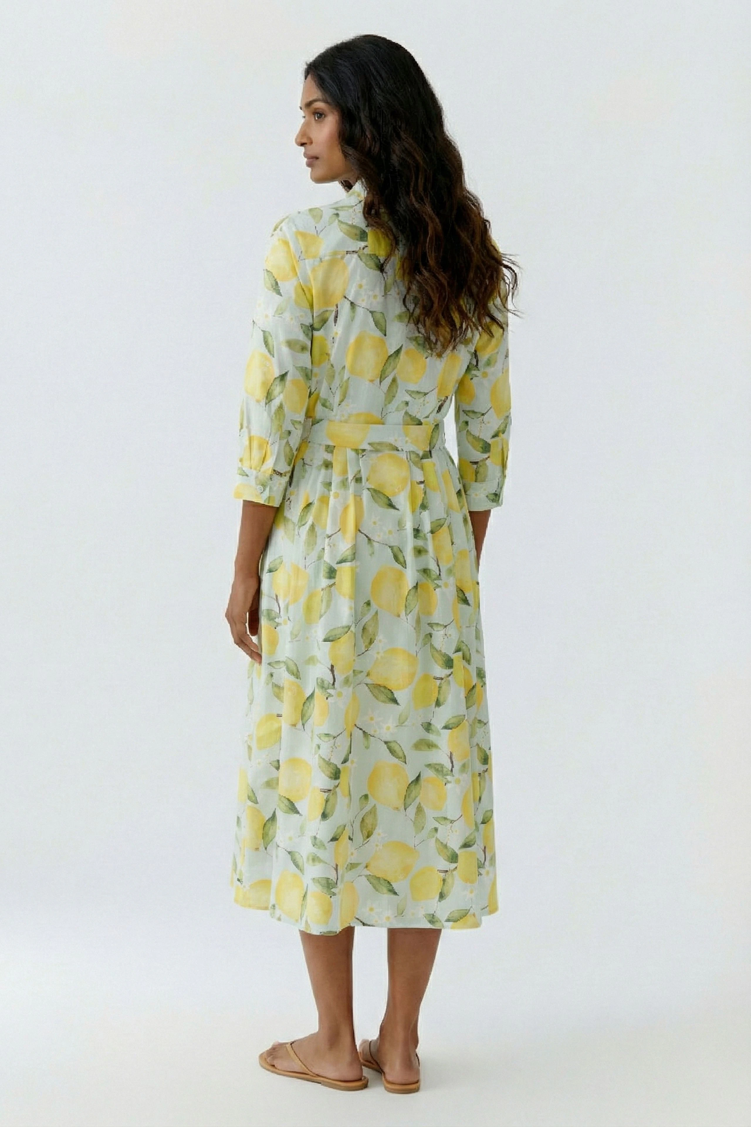 Frau im Midikleid mit Zitronenmuster, dreiviertel Ärmel, sommerlich und frisch, barfuß von hinten gezeigt.