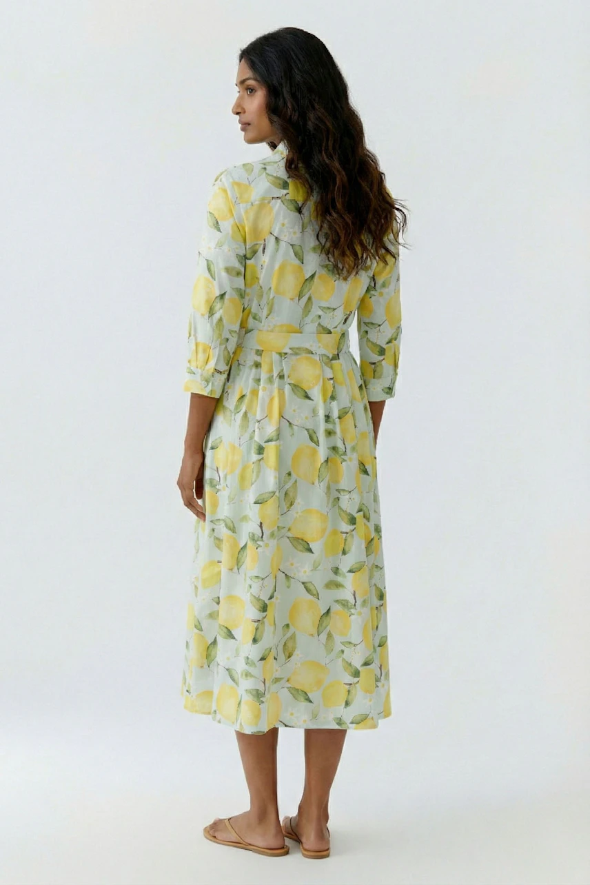Woman in lemon-patterned midi dress, long sleeves, standing barefoot, looking away.