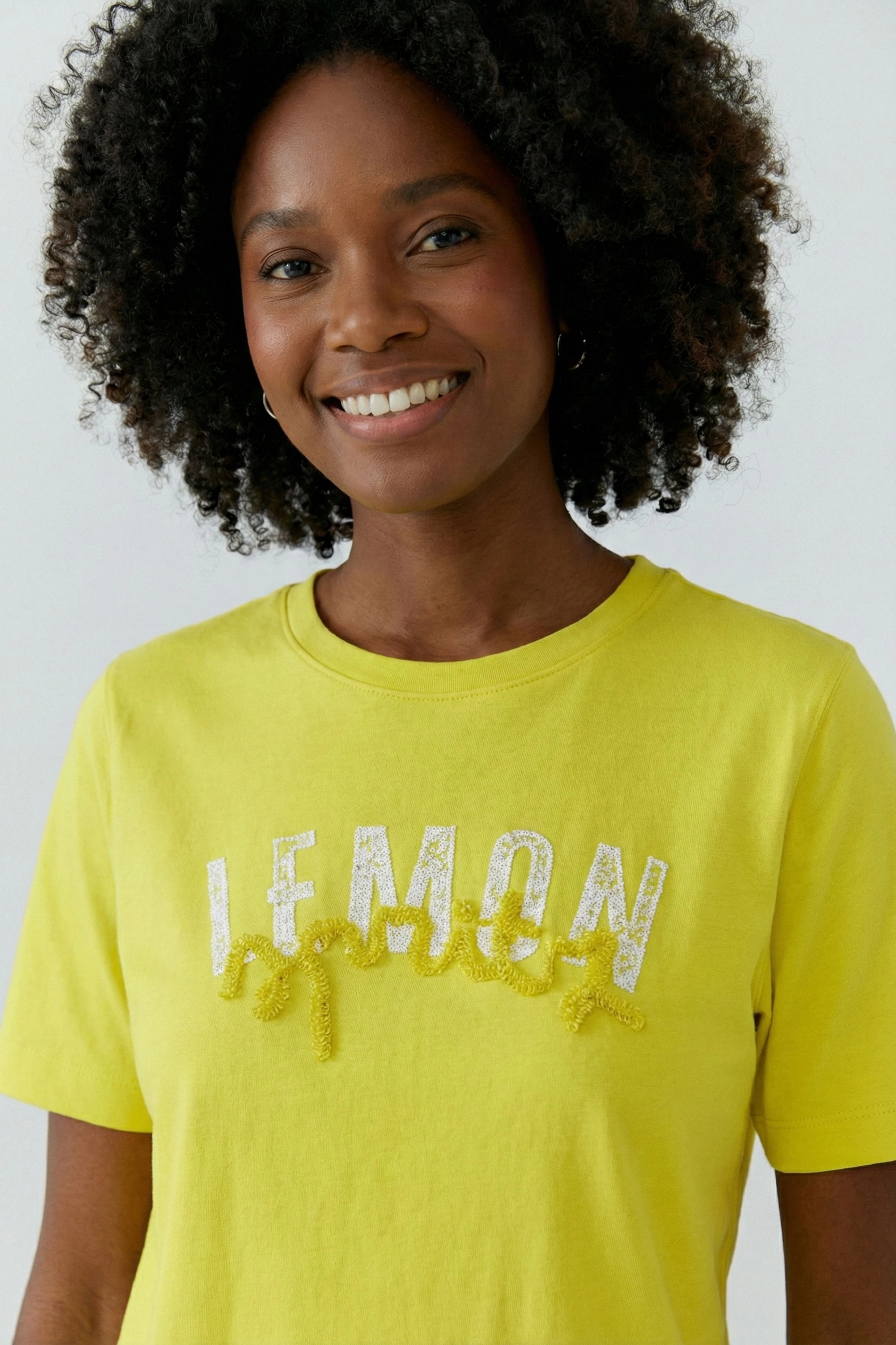 Gelbes Damen-T-Shirt: Frau im T-Shirt mit "LEMON"-Schriftzug, lächelt freundlich.