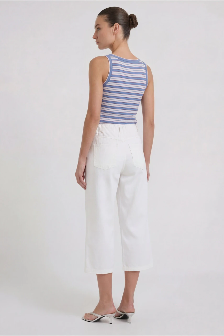 Casual culotte: Woman in white culottes and striped tank top, standing confidently.