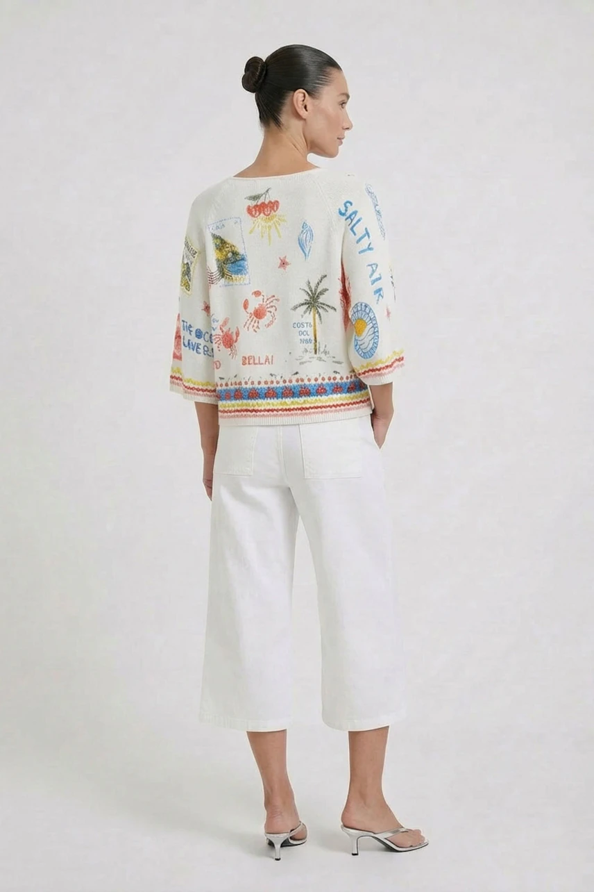 Frau im bunten Pullover mit sommerlichen Motiven, kombiniert mit weißen Hosen, von hinten zu sehen.