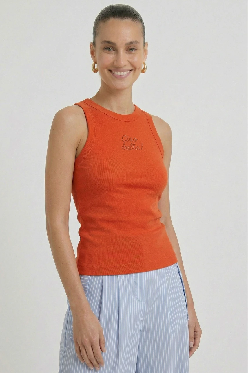 Woman in orange tank top with text, paired with light blue striped pants, smiling confidently.