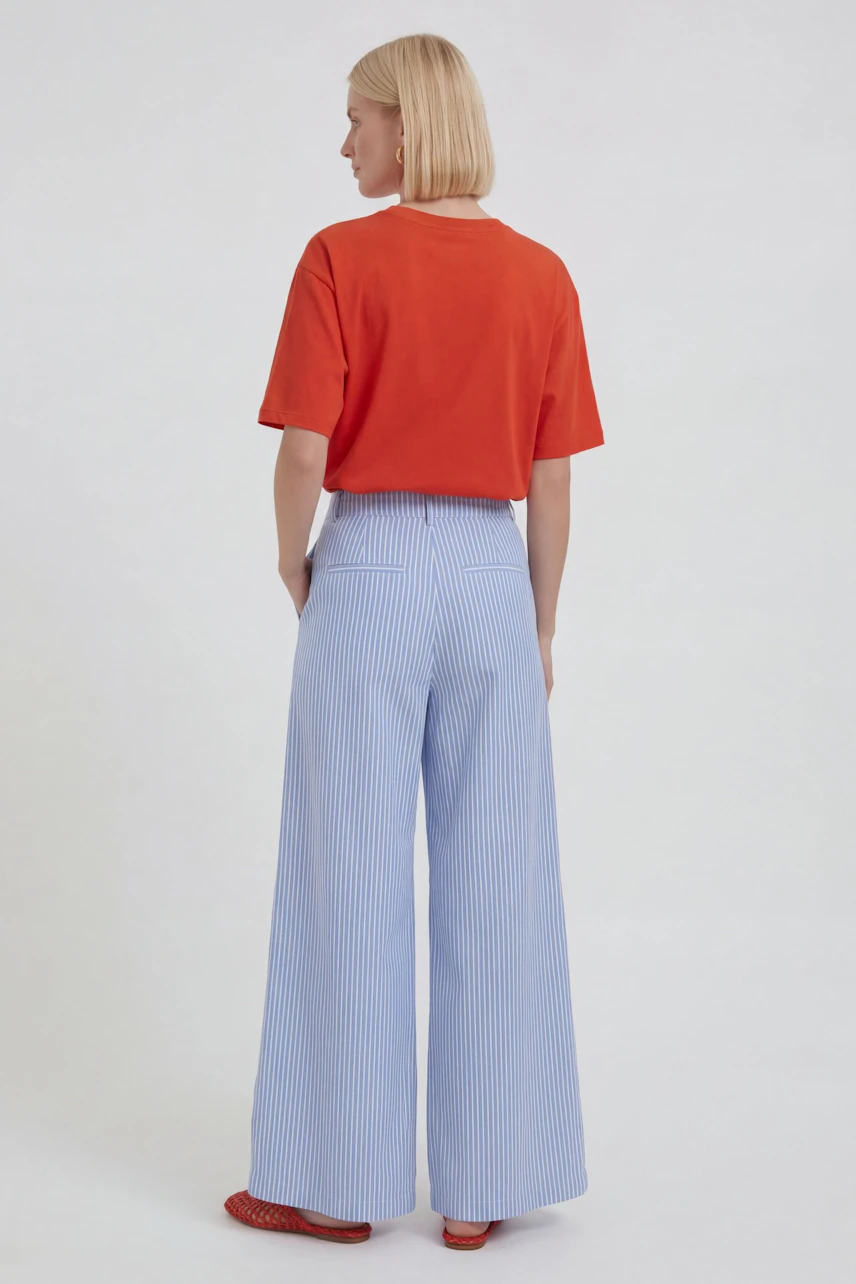 Woman in striped Marlene pants and red top, viewed from behind, showcasing relaxed fit and style.