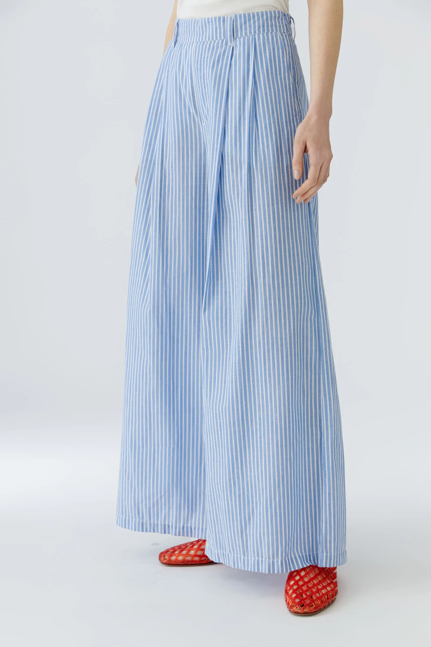 Woman in blue striped Marlene pants, white top, and red shoes, showcasing a relaxed, stylish look.