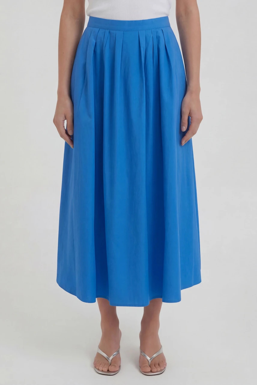 Blue midi skirt: Woman in a bright blue midirock with a white top and sandals, standing confidently.