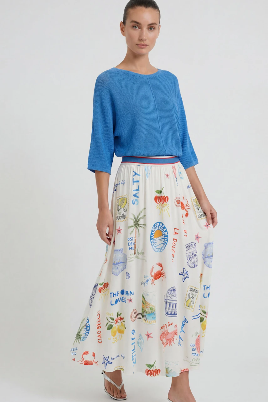 Frau im bunten Maxirock mit maritimen Motiven, kombiniert mit blauem Pullover. Sommerlich und frisch.