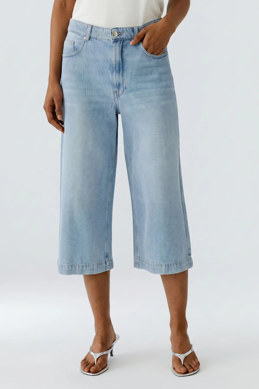 Casual culotte: Woman in light blue denim culottes and white top, standing confidently.