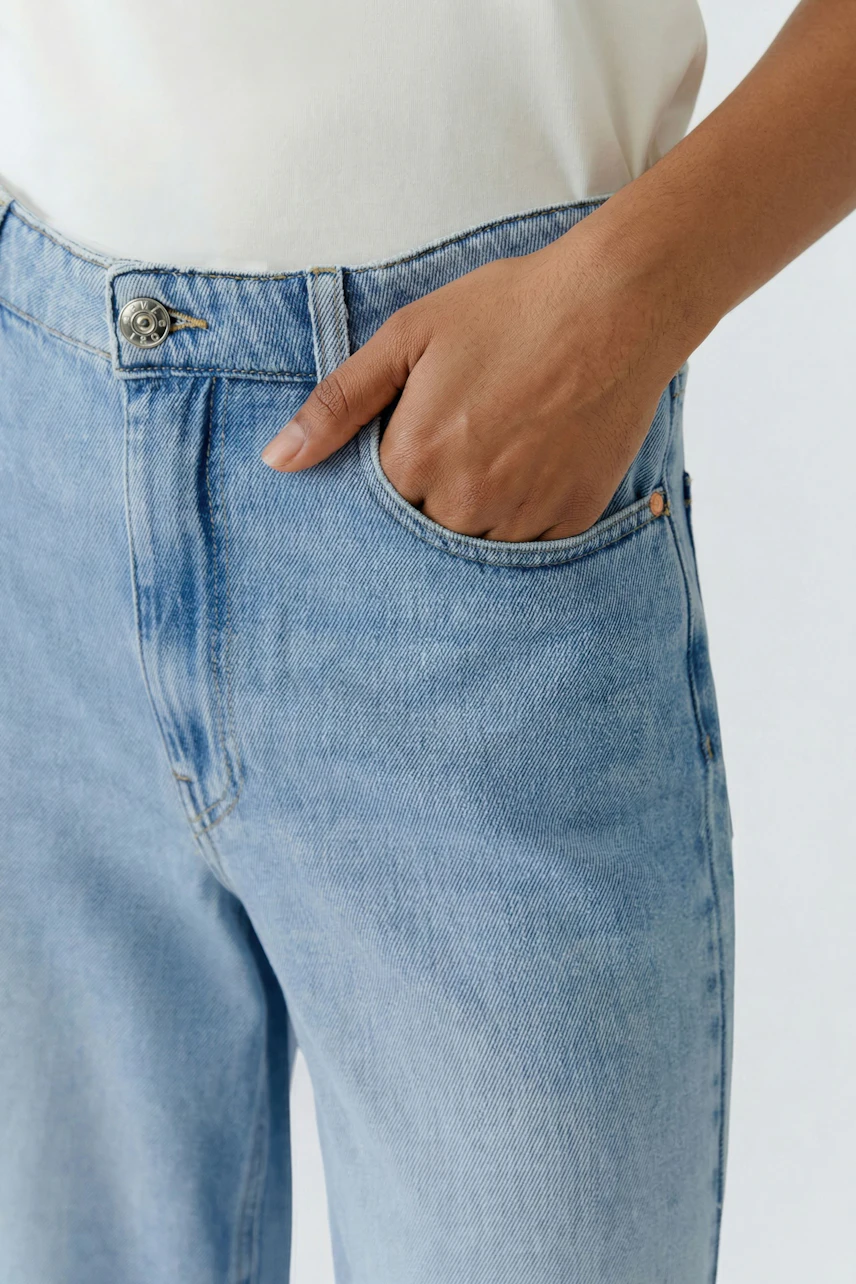 Casual culotte: Woman in light blue denim culotte with hand in pocket, showcasing relaxed style.