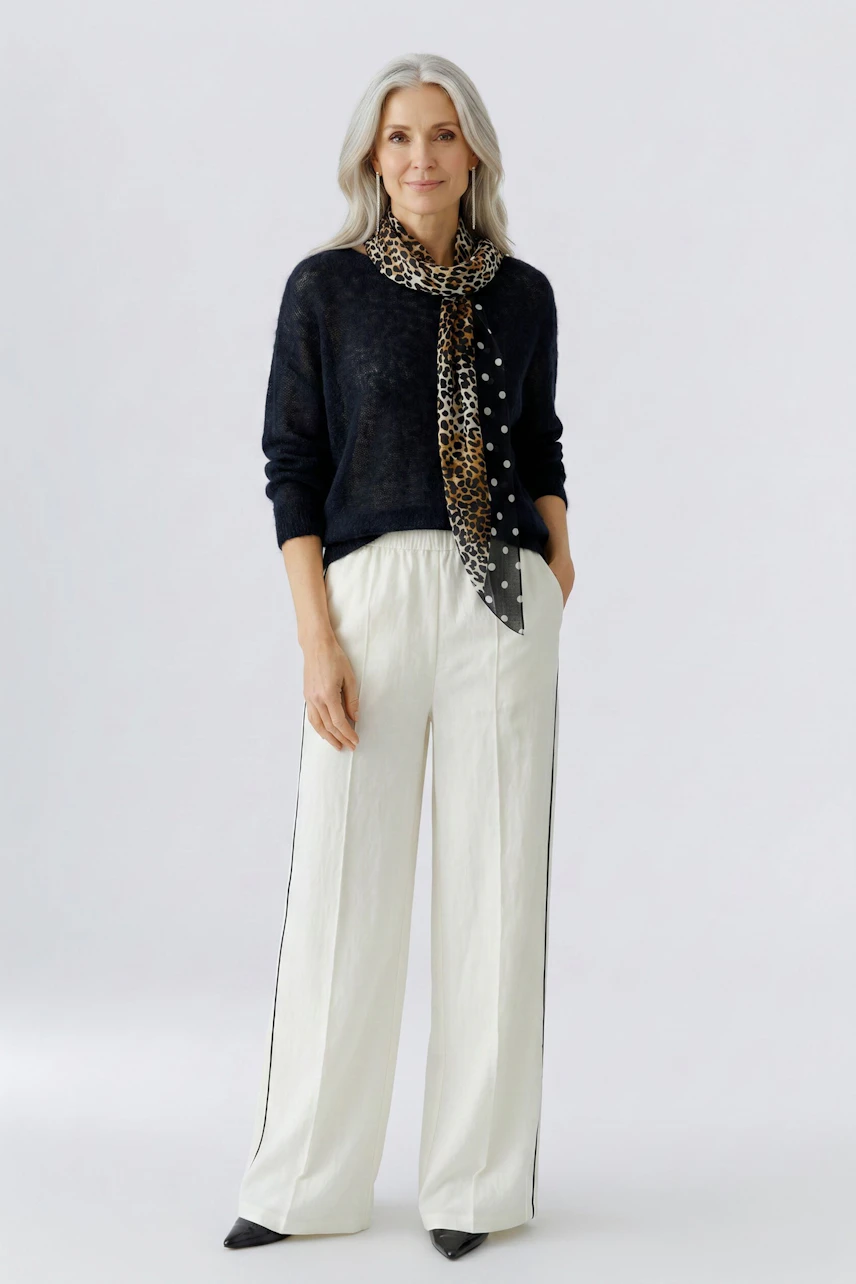 Stylish scarf: Woman in black pullover and white pants with leopard print scarf, hands in pockets.