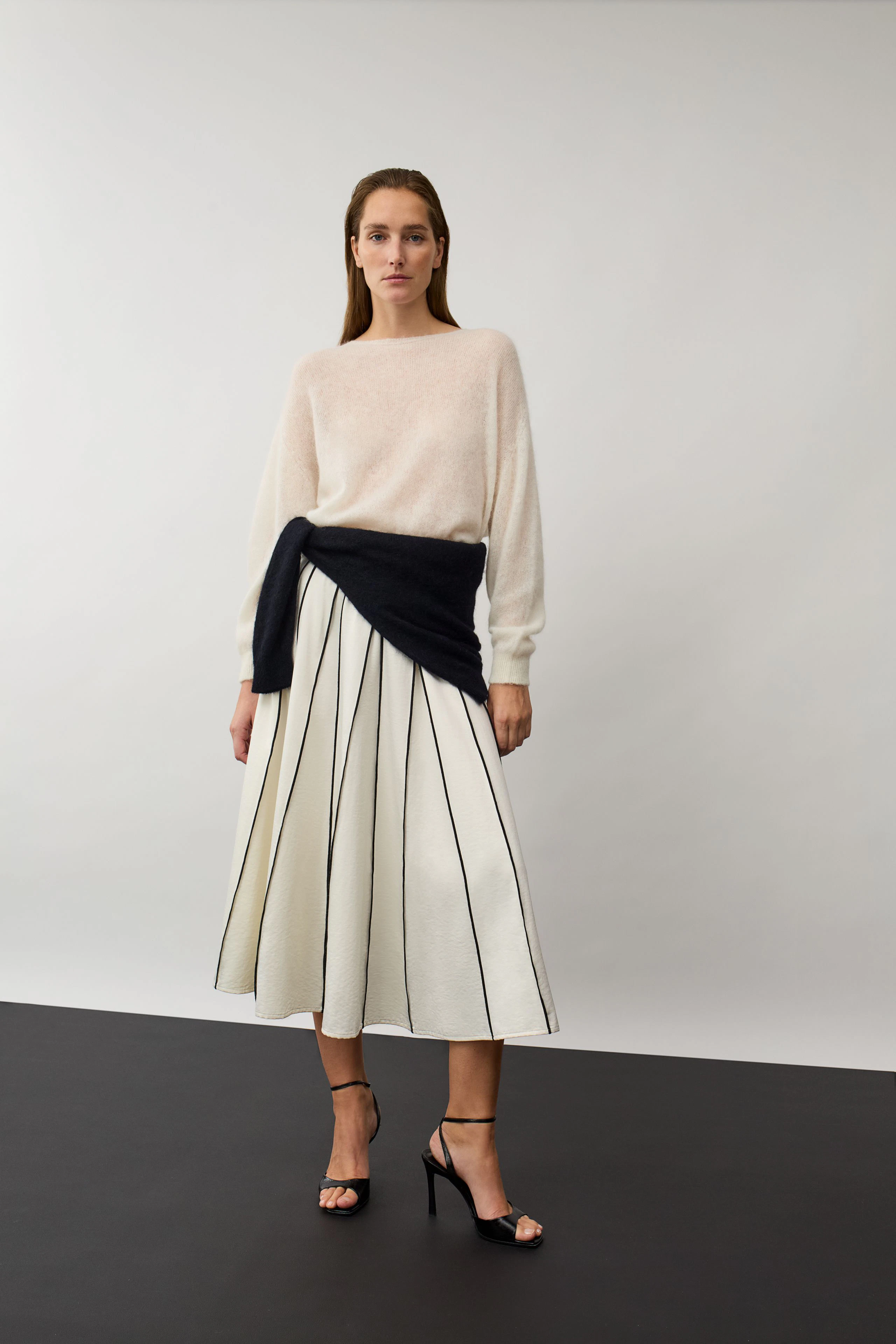Damen-Pullover: Frau im cremefarbenen Pullover, schwarzer Pullover um die Taille, gestreifter Rock.