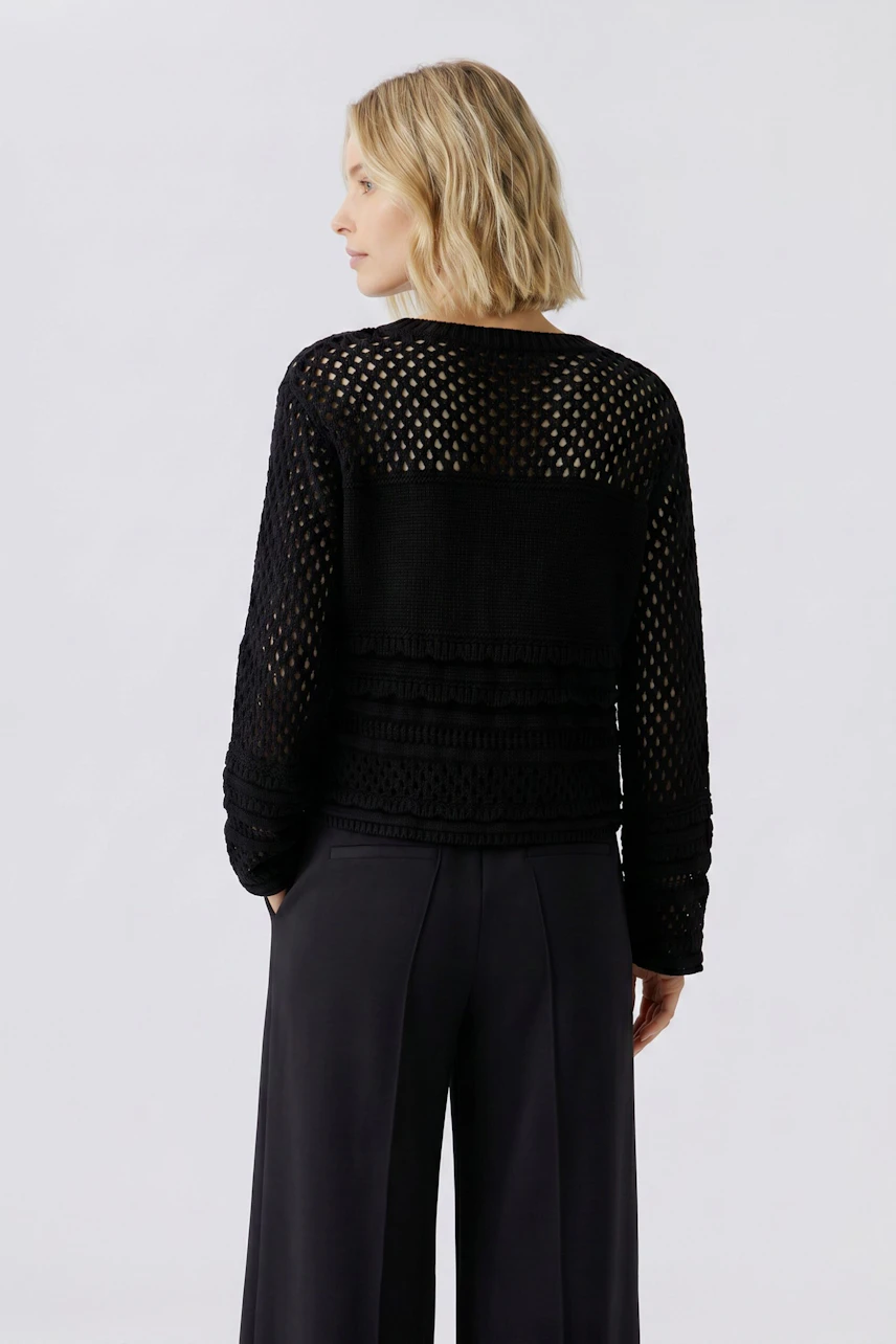 Woman in black pullover with mesh design and sequin details, paired with wide-leg pants.