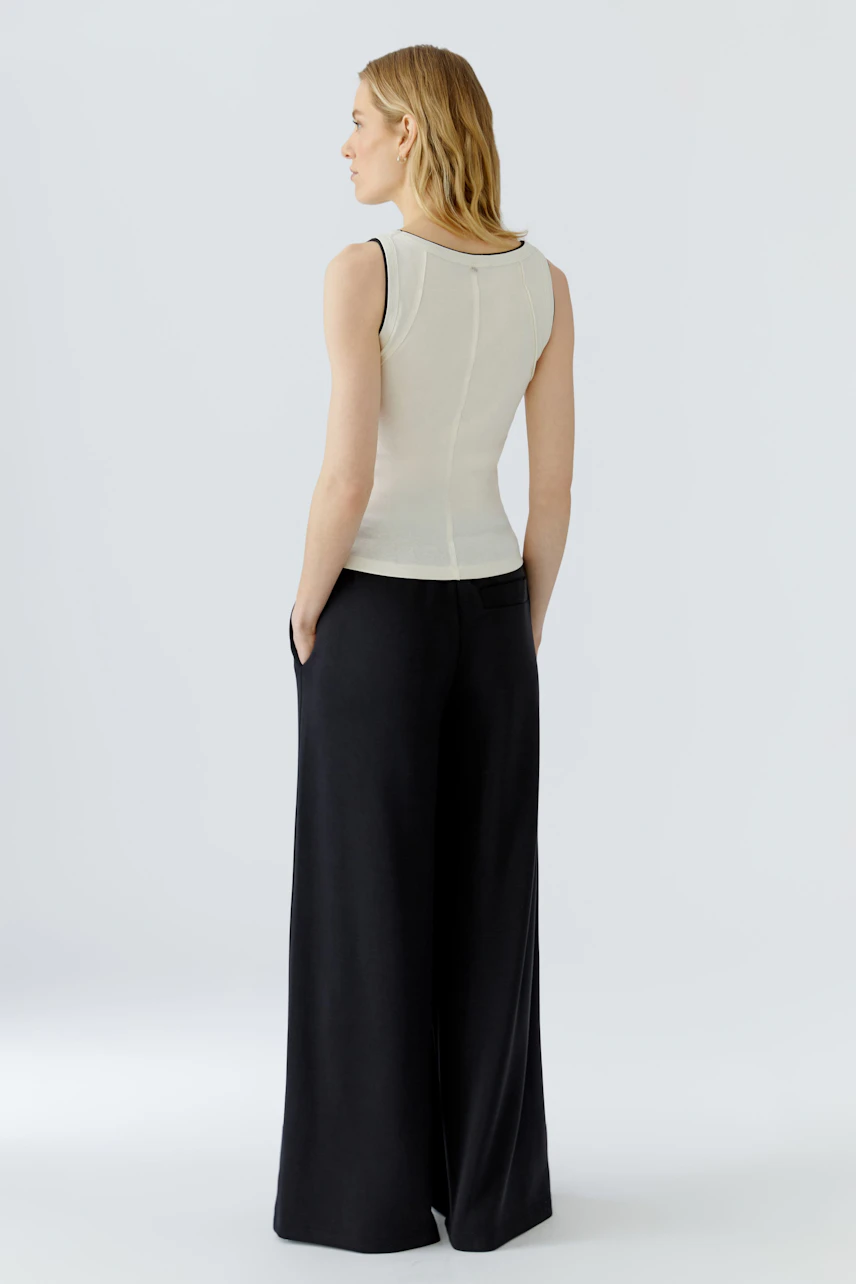 Woman in a white tank top and black wide-leg pants, viewed from the back, showcasing casual style.