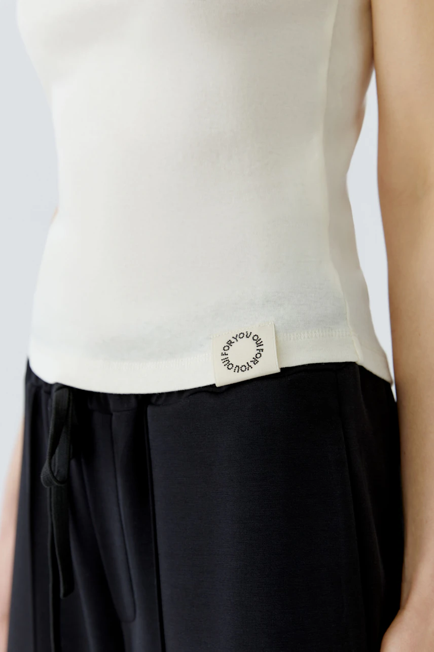 Woman in a white tank top and black pants, showcasing a casual and modern style.