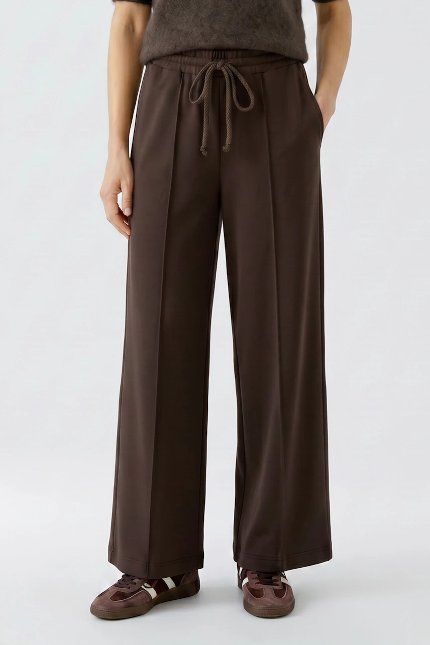 Woman in brown Marlene trousers, relaxed fit, drawstring waist, paired with casual sneakers.