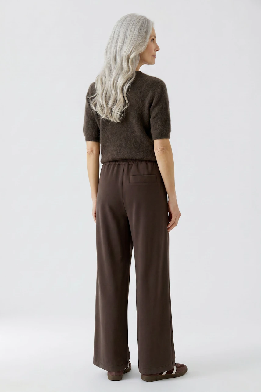 Woman in brown Marlene trousers and fuzzy pullover, standing confidently with long gray hair.