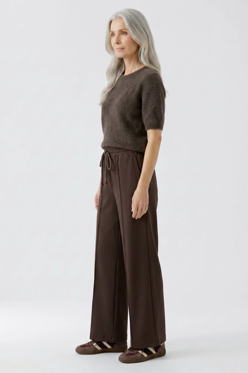 Woman in brown Marlene trousers and fuzzy top, standing confidently. Casual and stylish look.