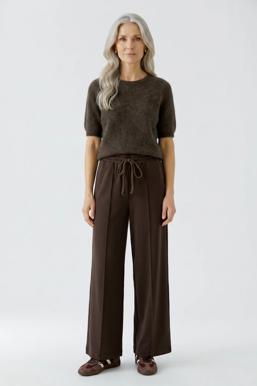 Woman in brown Marlene trousers and dark pullover, standing confidently.