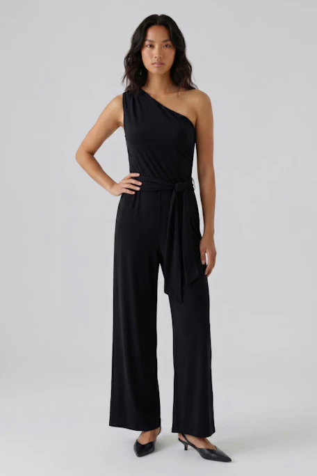 Black one-shoulder jumpsuit with waist tie, displayed on hanger. Simple and stylish design.