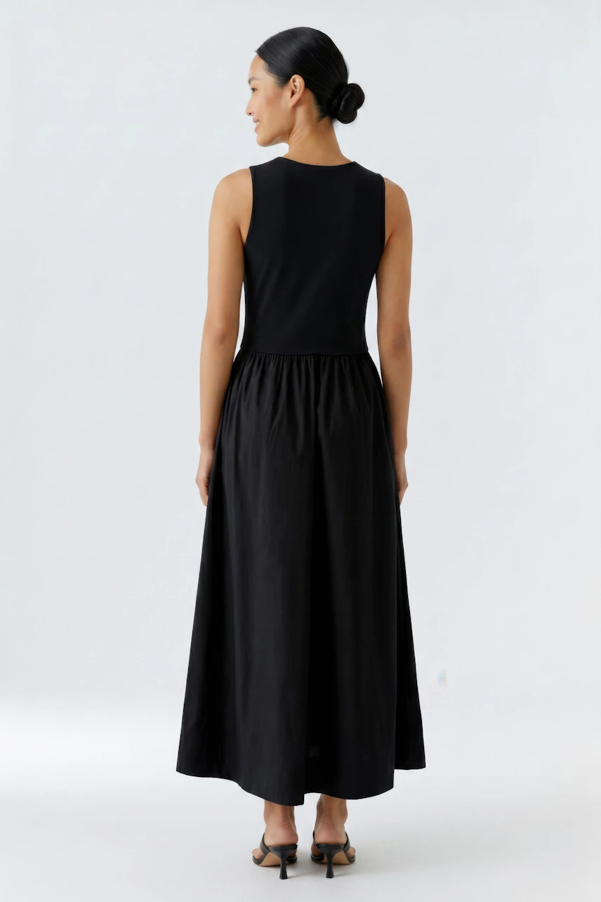 Woman in black sleeveless midi dress, standing with back view, showcasing flowy skirt and simple design.