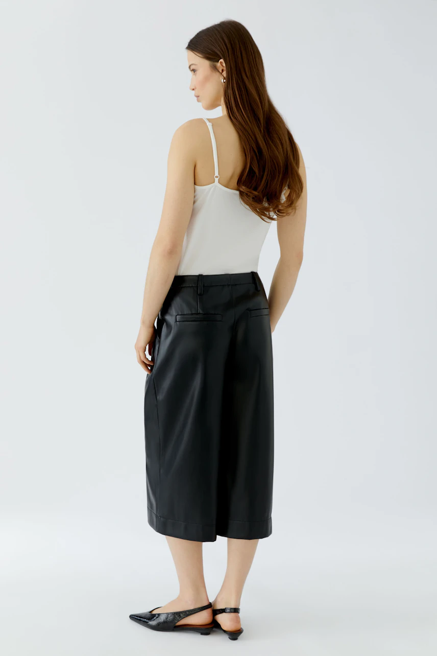 Woman in pleated trousers: Model in black pleated trousers and white top, viewed from the back.
