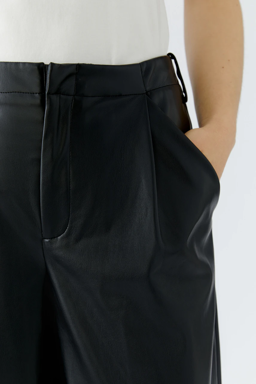 Woman in black pleated trousers with hands in pockets, wearing a white top. Casual and stylish look.