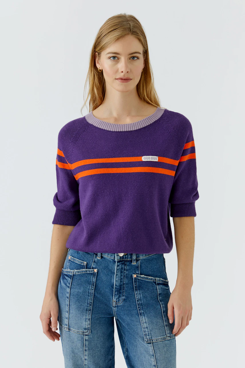 Lässiger Damen-Pullover: Frau im lila Pullover mit orangefarbenen Streifen und blauen Jeans.
