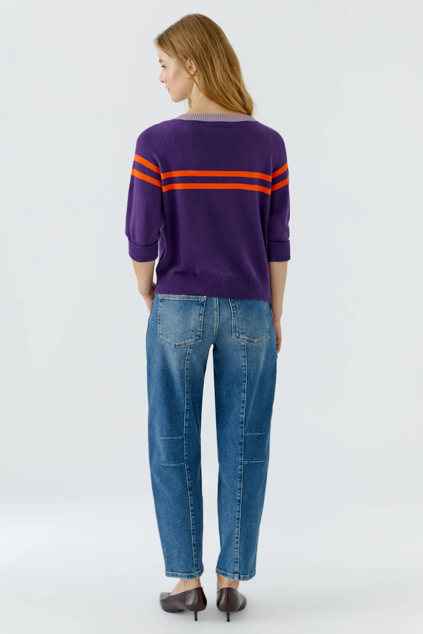Lässiger Damen-Pullover: Frau im lila Pullover mit orangefarbenen Streifen und blauer Jeans von hinten.