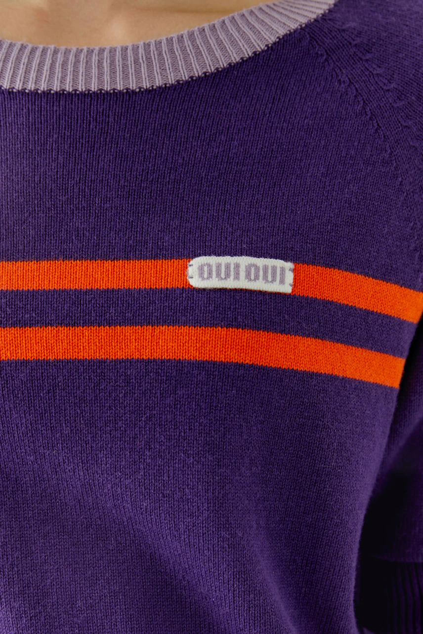 Lila Pullover mit orangefarbenen Streifen und Oui-Logo, getragen von einer Frau.